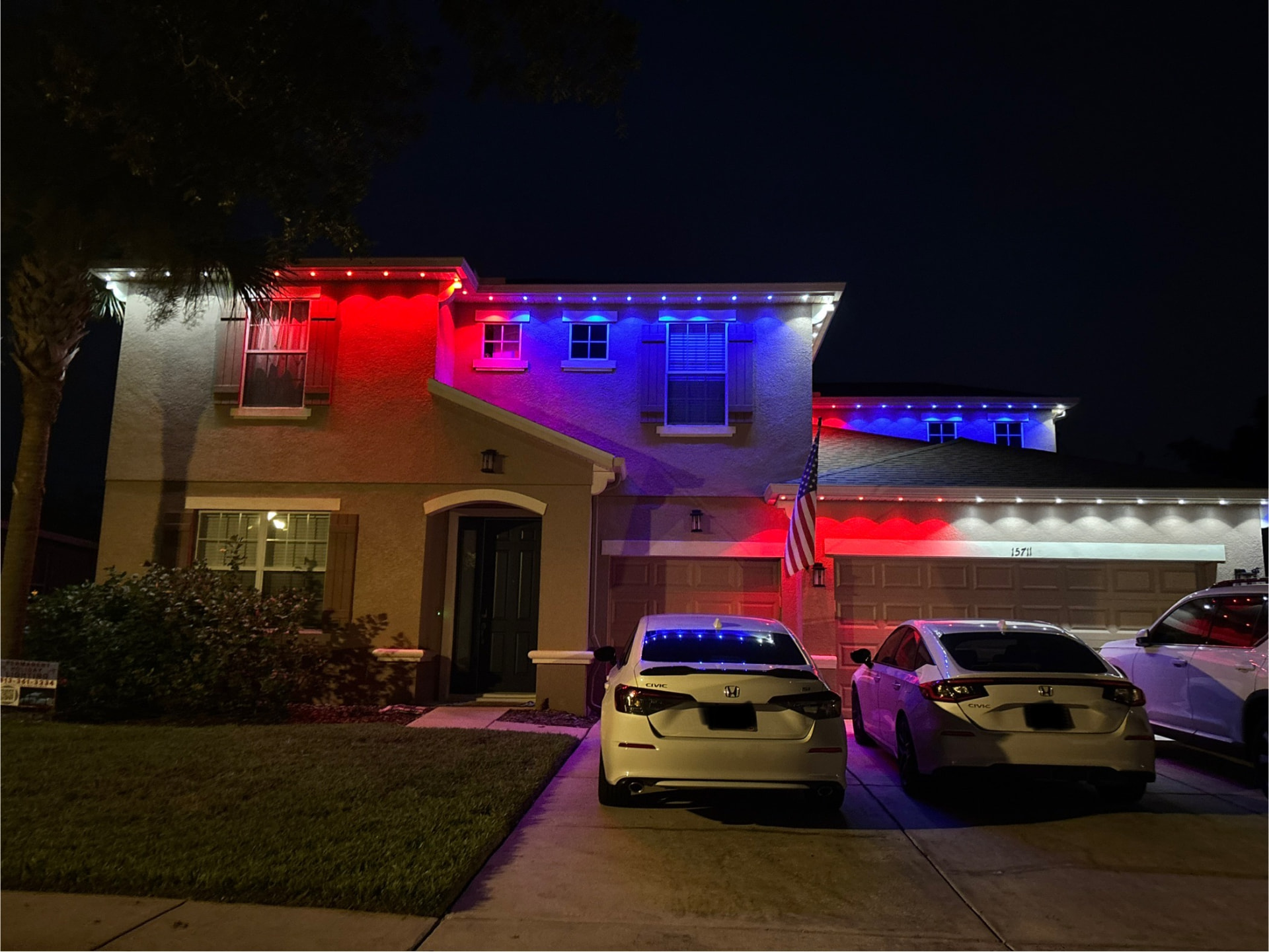 Stucco home at night with red, white and blue roofline lighting