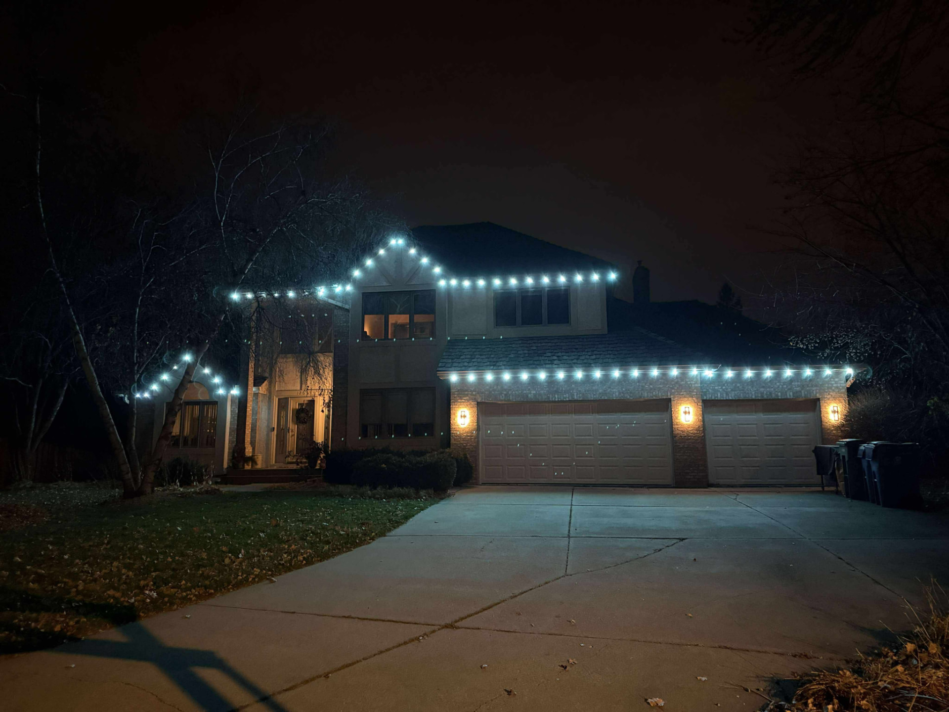 Large two-story home at night with white roofline lights and warm garage pillar lights